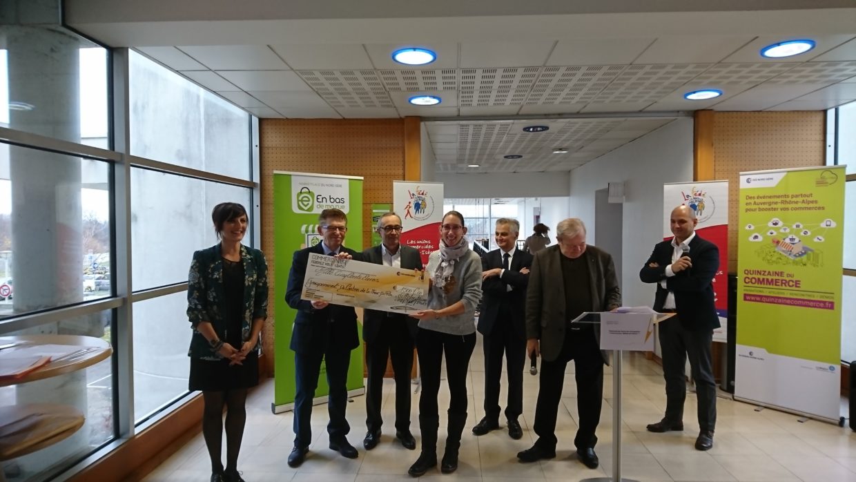 Un groupe de personne pose avec un chèque en papier. Tous ont le sourire et regarde le public derrière l'objectif.
2 femmes sont présentes sur la photo, et 5 hommes