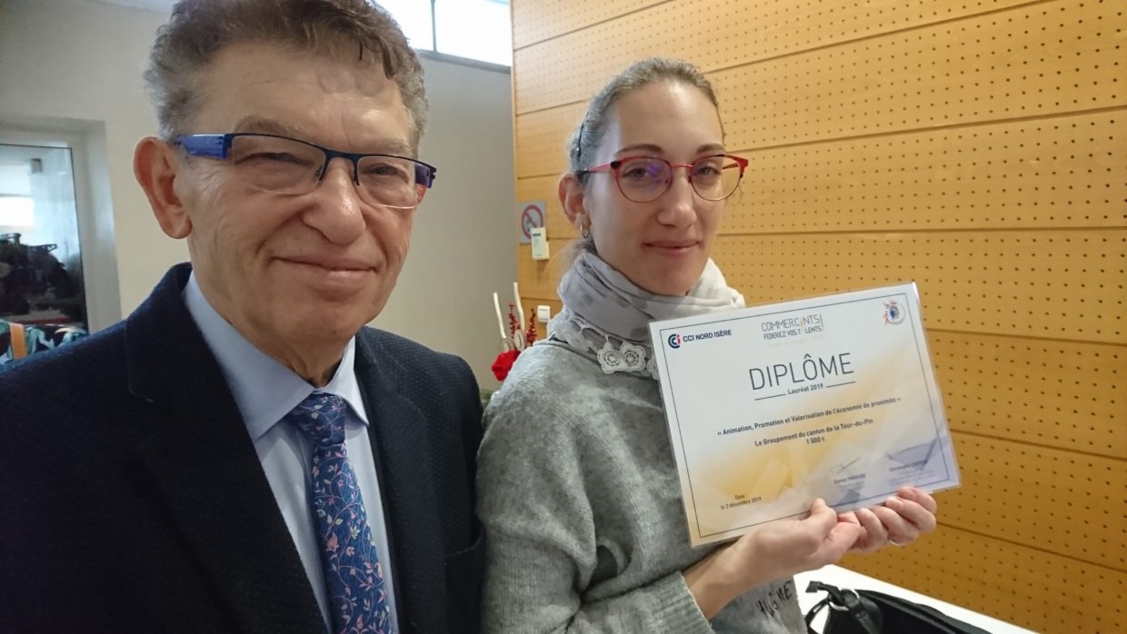 Un homme et une femme sont sur la photo. Ils portent tous les deux des lunettes et regardent en souriant l'objectif.
La femme tient entre les mains un document plastifié sur lequel la mention DIPLÔME apparait.
L'homme porte une cravate bleue avec des petites fleurs.